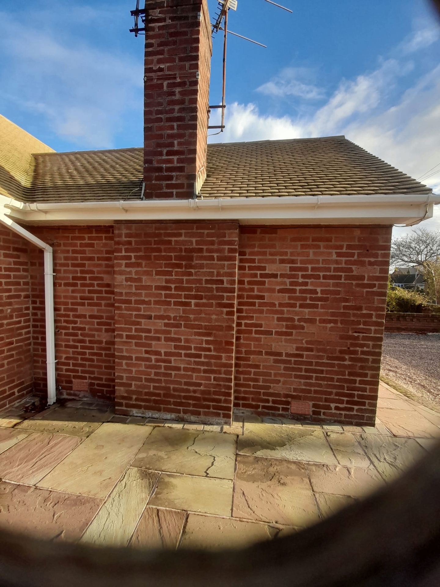 Red brick chimney and pitched tile roof with sandstone patio